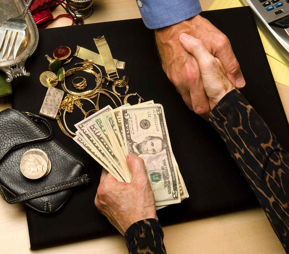 A close up of a woman shaking a jeweler's hand and receiving cash after selling gold