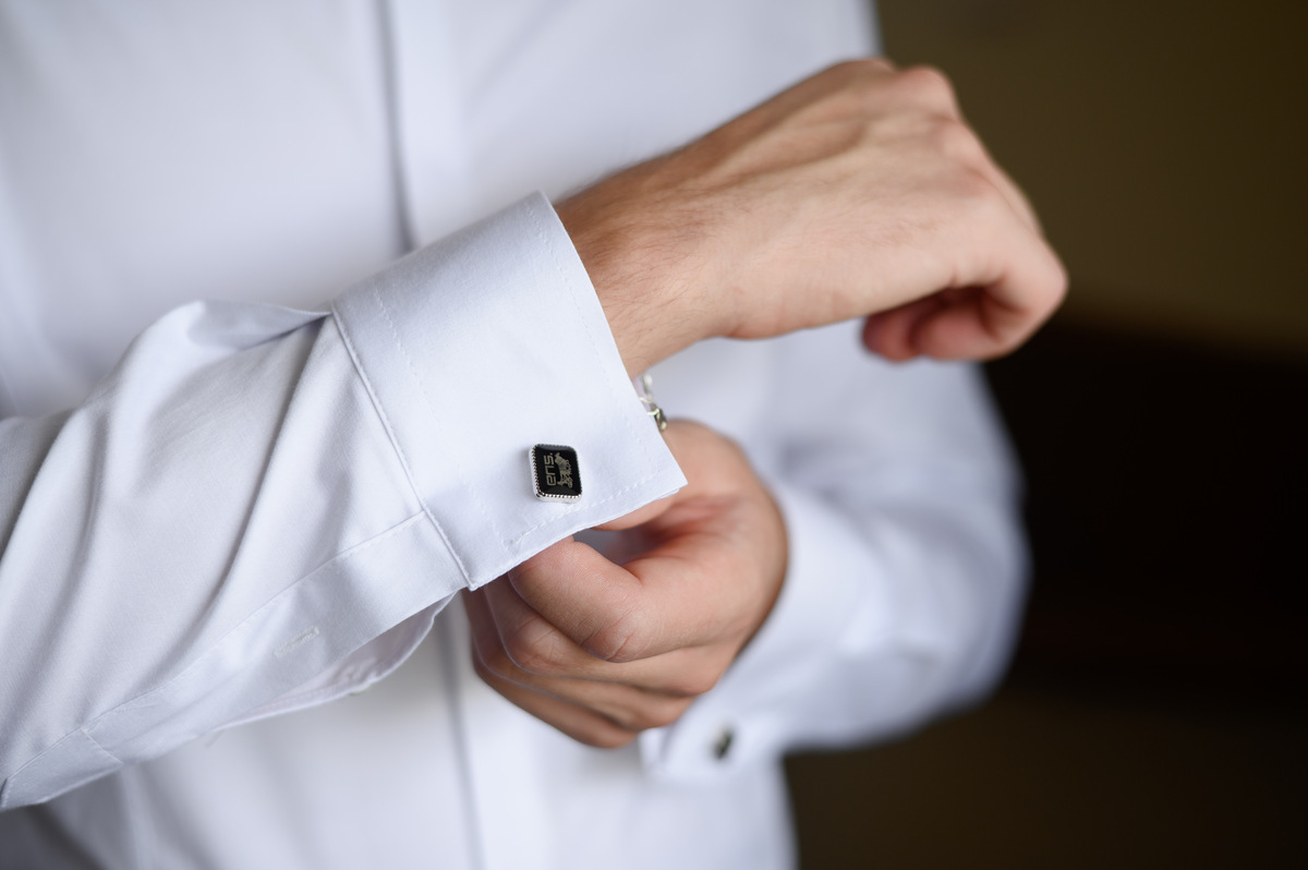 A closeup of a man in a white dress shirt adjusting his cuffs, which are held together by a pair of luxury cufflinks